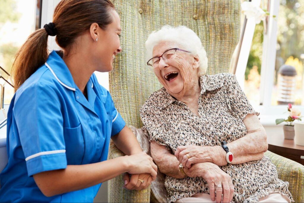 A senior woman and her caregiver in memory care sitting outside and laughing.