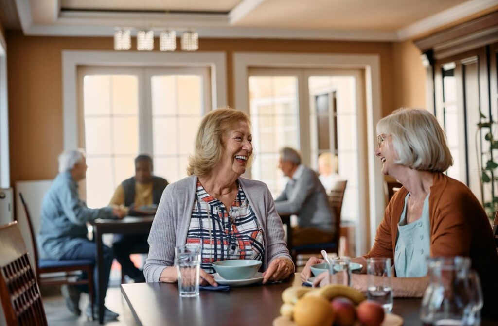 A couple of smiling seniors enjoy a meal together in their community's communal dining area.