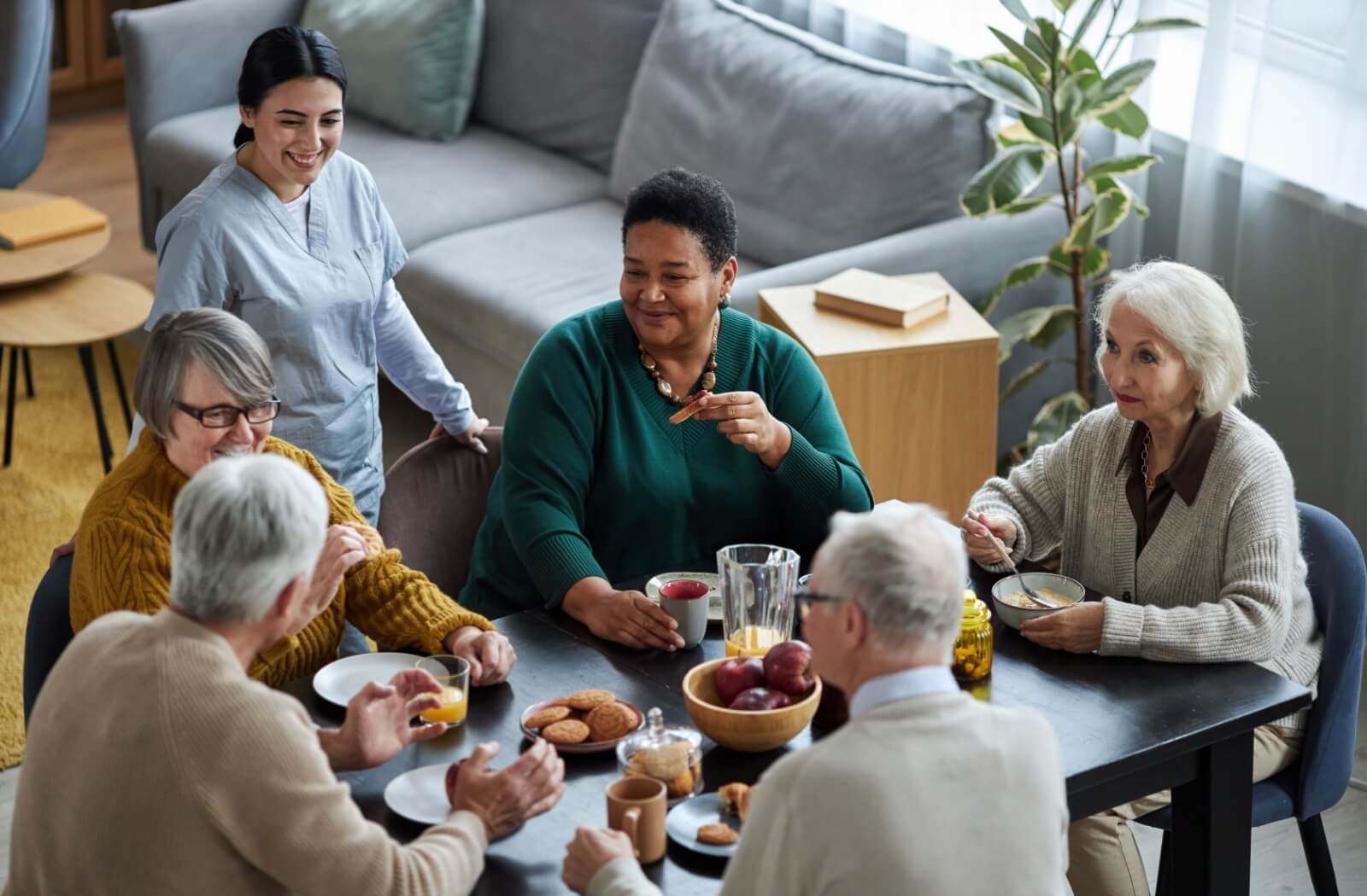 A vibrant group of senior living residents enjoy a shared meal while connecting with a staff member.