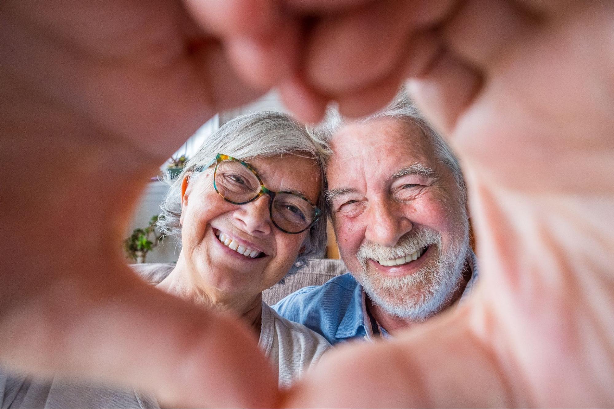 A happy senior couple laughing and making a heart together with their hands while out on a day trip.