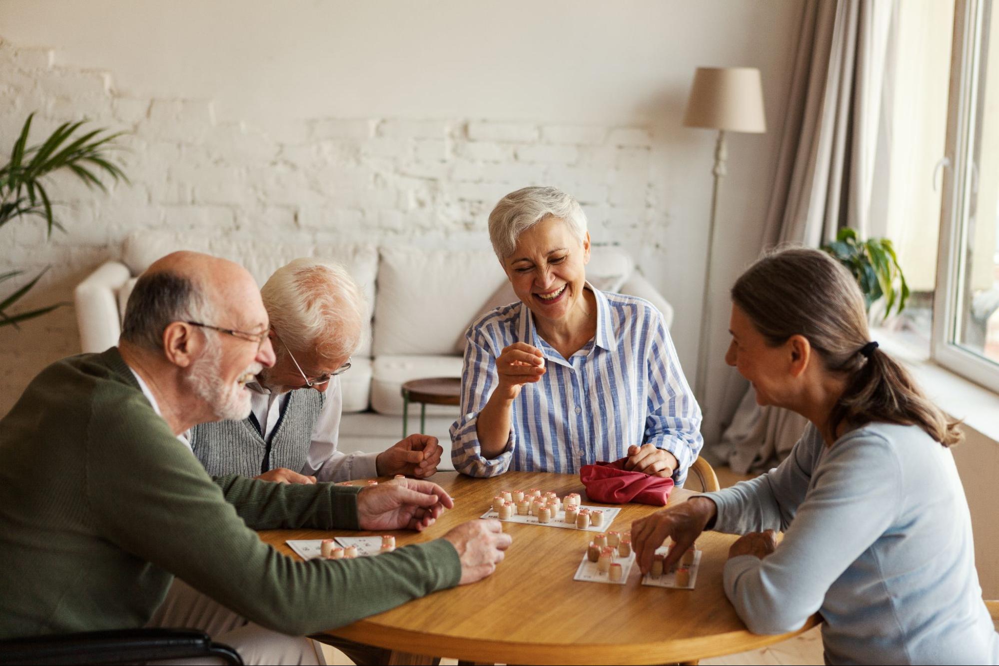 A group of seniors in memory care laughing around a table while playing a board game.