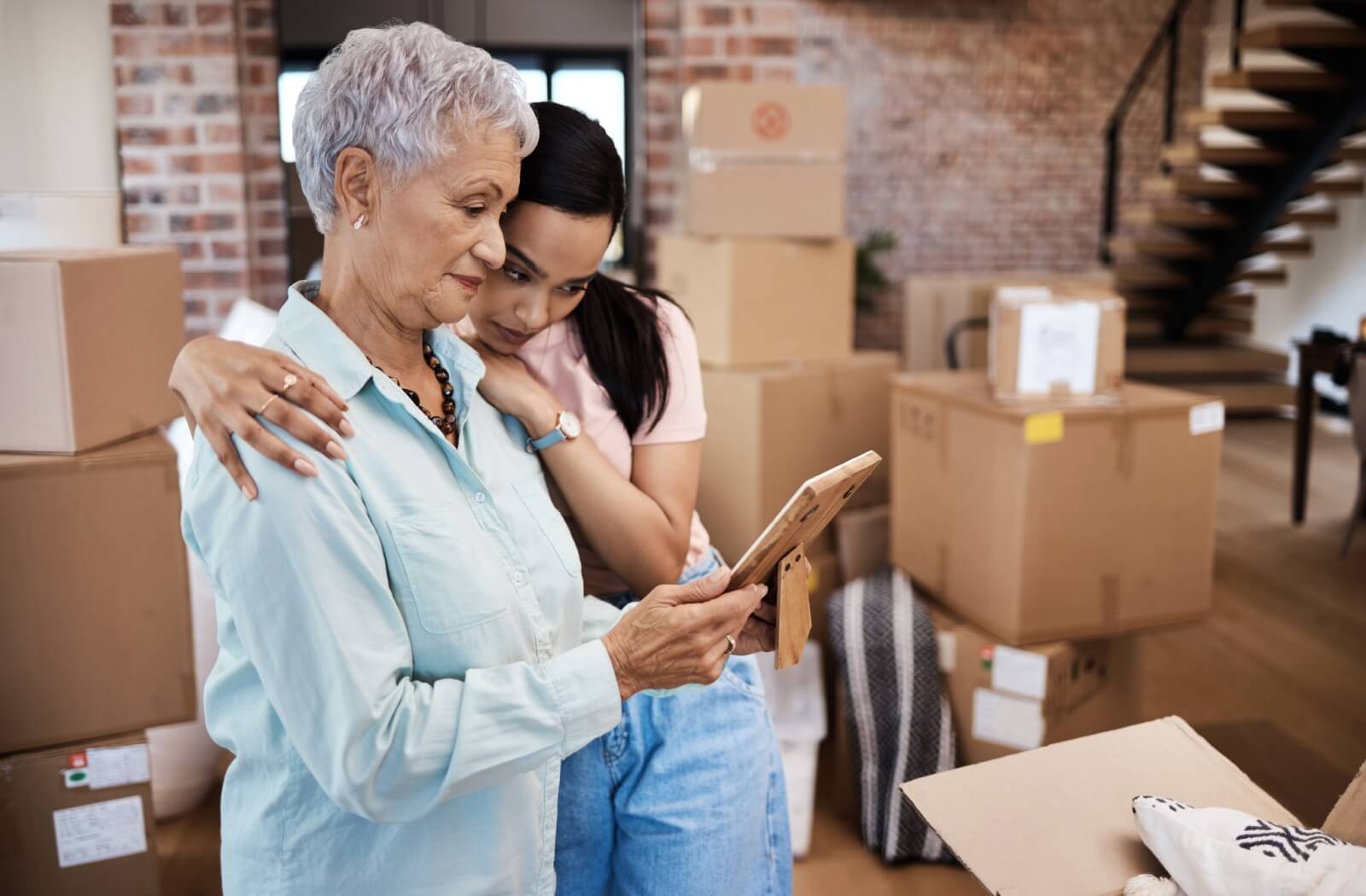 An adult child and their senior parent reminicse over a photograph as they pack for the move to assisted living.