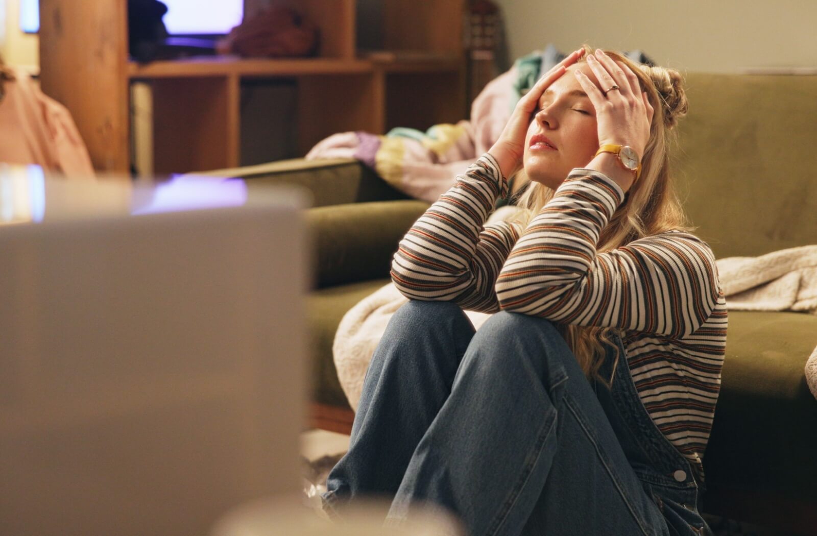 An overwhelmed person sits on the floor and holds their head.