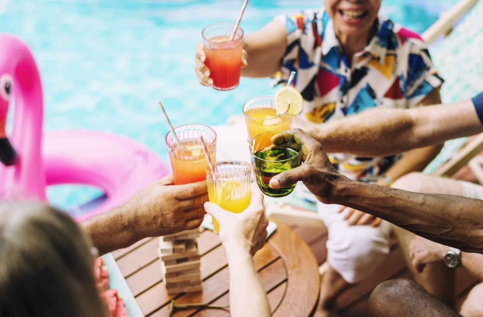 Group of seniors toasting with colorful mocktails beside a pool during a cheerful summer gathering