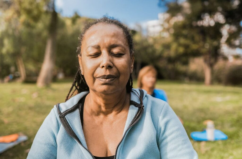 Senior with eyes closed during outdoor meditation or yoga session in a grassy park setting on a sunny day